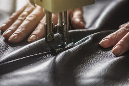 Women's hands in the process of sewing on professional equipment. Sewing leather in production. Close-up.の写真素材