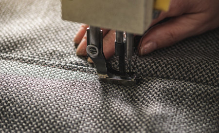 Women's hands in the process of sewing on professional equipment. Sewing fabric in production. Close-up.の写真素材
