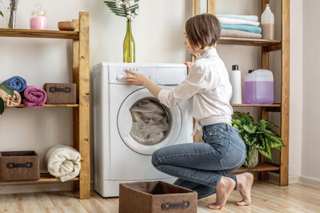 A woman is washing clothes in a washing machine in a laundry room. The concept of caring for things, cleaning and hygieneの写真素材