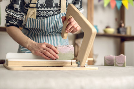 Women's hands cut homemade natural soap on a professional wood cutter. A means of eco-friendly hygiene and pleasant giftsの写真素材