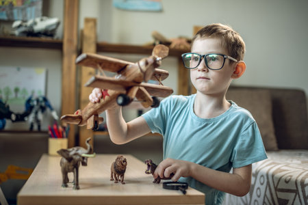 A child boy in the children's room is playing with a toy wooden airplane with animals of the savannah. Fantasies of great adventures and travels.の写真素材