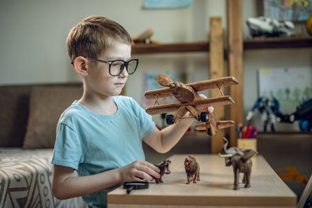 A child boy in the children's room is playing with a toy wooden airplane with animals of the savannah. Fantasies of great adventures and travels.の写真素材