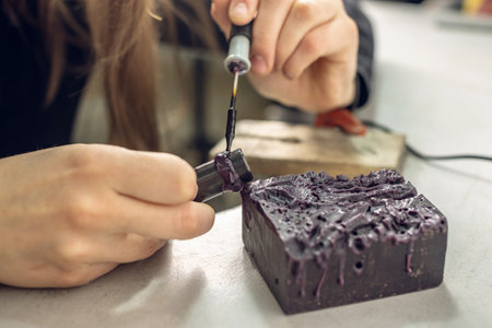 A female jeweler constructs a unique ring design using wax melting. Craft in a jewelry workshop.の写真素材