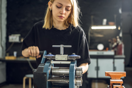A female jeweler rolls a piece of jewelry in the form of a silver ring with a press. Craft in a jewelry workshop.の写真素材