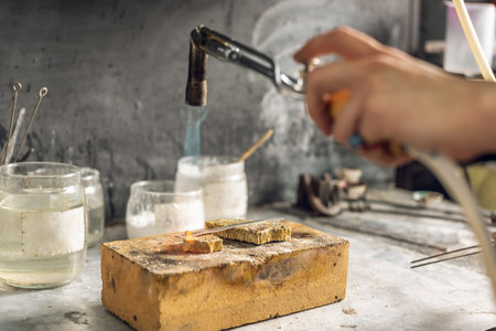 Heating with a flame jet of a metal billet of a silver ring. The work of a jeweler in the workshop