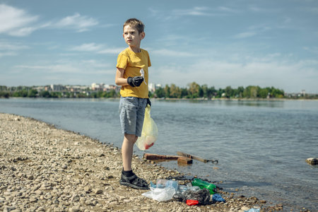A child boy volunteer in gloves tidying up rubbish plastic garbage from the riverbank. Children take care of nature.の写真素材