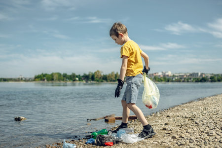 A child boy volunteer in gloves tidying up rubbish plastic garbage from the riverbank. Children take care of nature.の写真素材