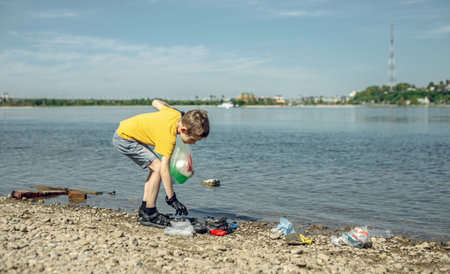 A child boy volunteer in gloves tidying up rubbish plastic garbage from the riverbank. Children take care of nature.の写真素材