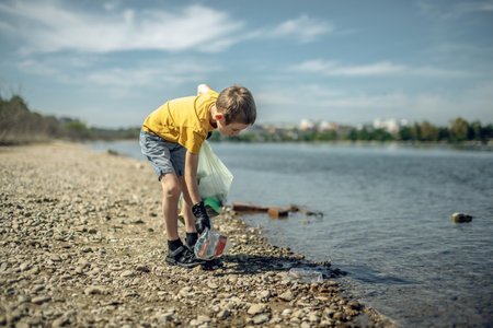A child boy volunteer in gloves tidying up rubbish plastic garbage from the riverbank. Children take care of nature.の写真素材