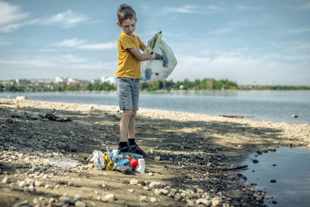 A child boy volunteer in gloves tidying up rubbish plastic garbage from the riverbank. Children take care of nature.の写真素材
