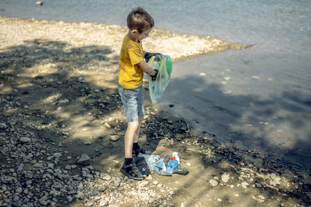 A child boy volunteer in gloves tidying up rubbish plastic garbage from the riverbank. Children take care of nature.の写真素材