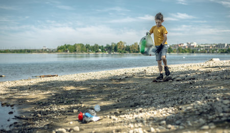 A child boy volunteer in gloves tidying up rubbish plastic garbage from the riverbank. Children take care of nature.の写真素材