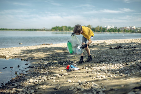 A child boy volunteer in gloves tidying up rubbish plastic garbage from the riverbank. Children take care of nature.の写真素材
