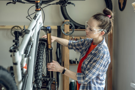 Young woman fixing a mountain bike in a repair shop. Concept of preparation for the new season, repair and maintenanceの写真素材