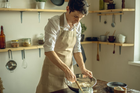 A baker in an apron kneads the dough with his hands and sprinkles it with flour to bake homemade...