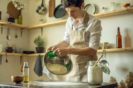 A baker in an apron kneads the dough with his hands and sprinkles it with flour to bake delicious homemade bread. Rustic style on a dark backgroundの写真素材