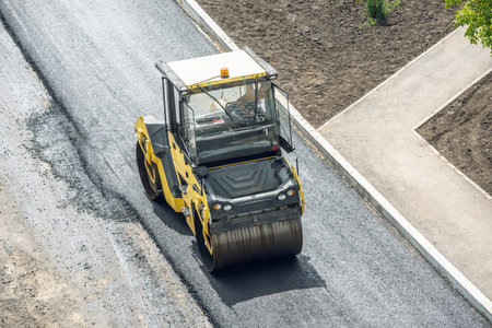 Workers lay a new asphalt coating using hot bitumen. Work of heavy machinery and paver. The view...
