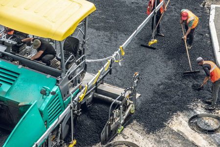 Workers lay a new asphalt coating using hot bitumen. Work of heavy machinery and paver. The view...