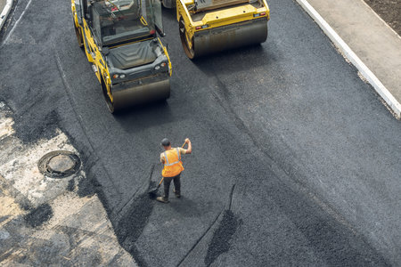 Workers lay a new asphalt coating using hot bitumen. Work of heavy machinery and paver. The view...