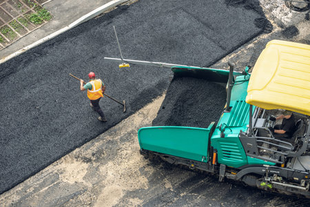 Workers lay a new asphalt coating using hot bitumen. Work of heavy machinery and paver. The view...