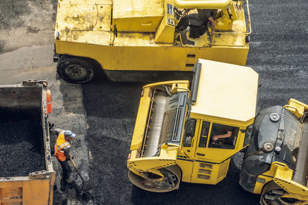 Workers lay a new asphalt coating using hot bitumen. Work of heavy machinery and paver. The view...