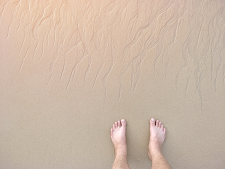 feet stand on the beach with sand pattern texture photo take from top viewの写真素材