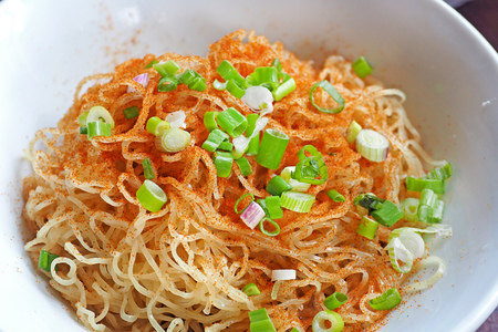 cooked dried noodles topped with paprika and green onion served on white ceramic bowlの写真素材