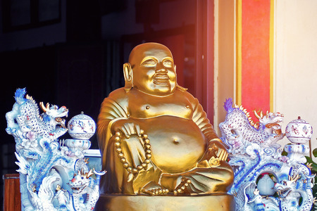 Fat chinese god statue at the front of chinese temple in gold color with the dragonの写真素材