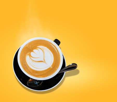 isolated on yellow background  of cup of coffee hot smoke latte art in heart shape served on black modern vintage cupの写真素材
