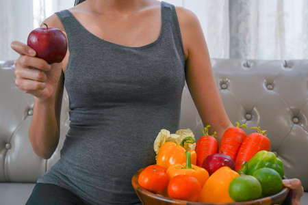 The healthy Asian pregnant young woman holds the apple with many kinds of fruit and vegetable.の写真素材