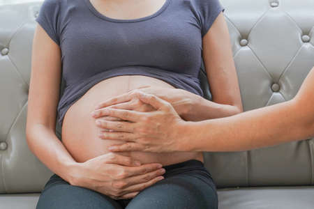A pregnant woman and hand of a husband touching her fetus with a warm love hand on her fetus. love mom loves the baby concept.の写真素材