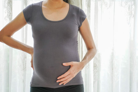 Close Up Picture of a pregnant woman standing with the window in the background at home.