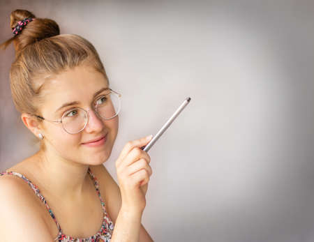 Portrait of a healthy young woman with glasses and a pencil in her hands at a table on a gray backgroundの写真素材