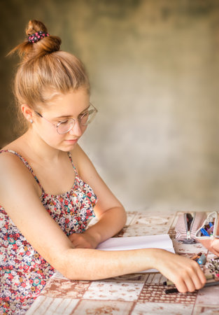 Portrait of a healthy young woman with glasses sitting at a table and looking at a notebook, on a gray backgroundの写真素材