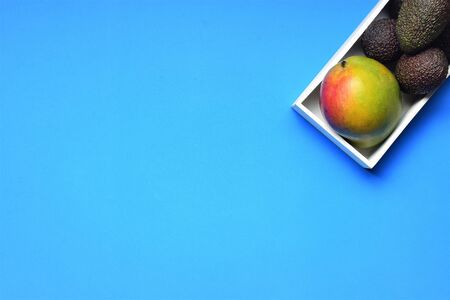 Mango and avocados in white box, on blue backgroundの写真素材