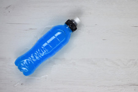 Bottle with isotonic drink on cloth, space for text on the wooden table