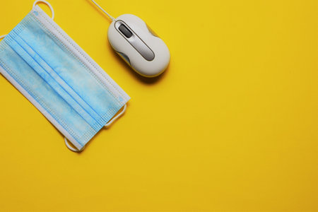 Wired PC mouse and surgical mask on yellow background, space for text