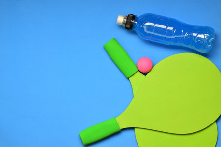 Beach rackets and isotonic drink on blue background, space for text