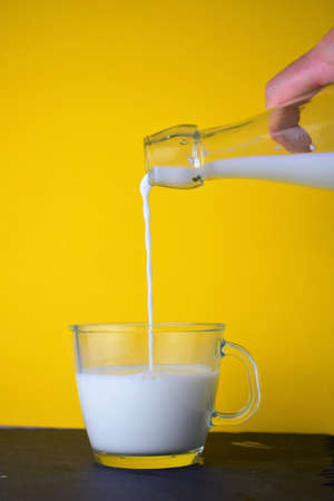 Pouring milk from the bottle into the glass, with a yellow backgroundの写真素材