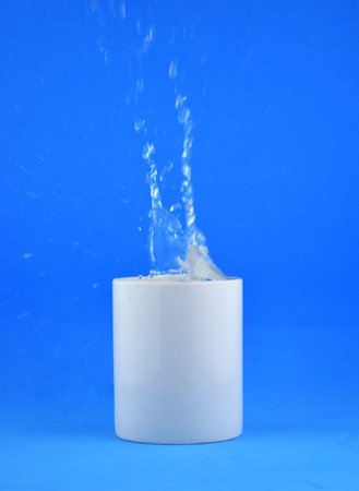 As main shot, white porcelain cup on blue background, splash