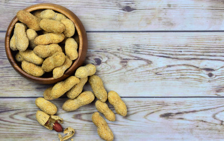 Group of peanuts, next to a bowl and on wooden boards, space for text