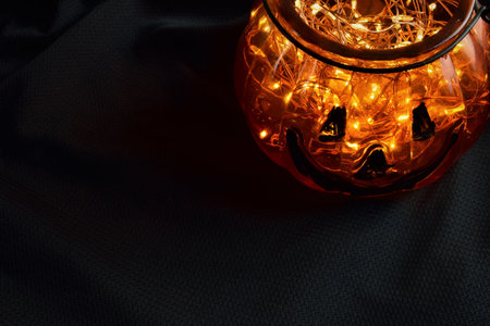 Glass halloween pumpkin with little lights inside, dark background, space for text