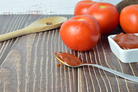 Close up metal spoon with tomato sauce, on wooden board.の写真素材