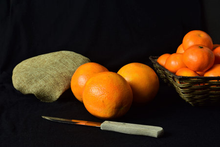Citrus. Close up, orange on dark background, on the side set of tangerines in wicker basket