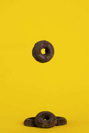 Chocolate covered cookies, one of them suspended in the air and the rest in a group, on a yellow backgroundの写真素材