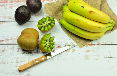 Assorted tropical fruit, kiwis, bananas and avocados on white boards.