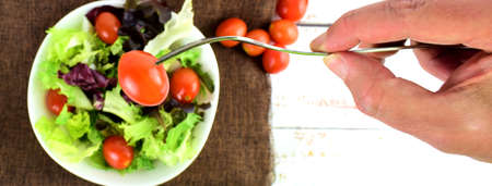 Close up, picking a cherry tomato with the fork, from the white bowl, with a variety of salad.の写真素材