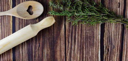 On rustic wooden table, kitchen utensils with stems of aromatic plant, rosemary. Copy space.の写真素材