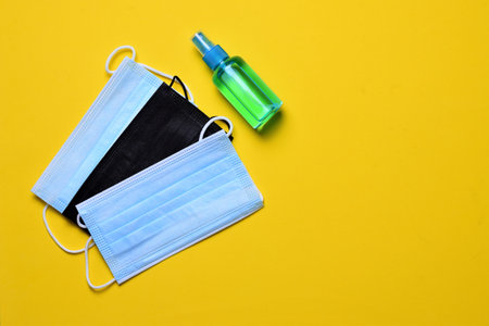 Hygienic and sanitary measures. Hand sanitizer gel and surgical mask on yellow background.