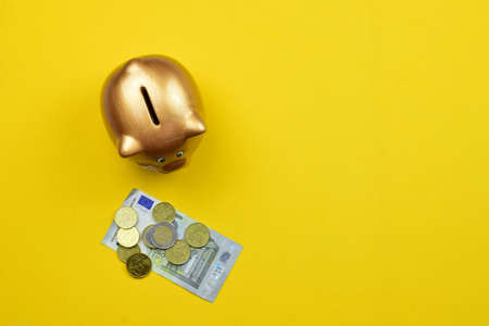 On yellow background piggy bank, coins and euro bill, economy concept. Zenith view and copy space.の写真素材
